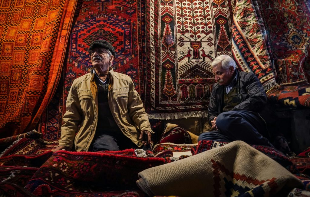 A couple of men sitting on top of a pile of rugs